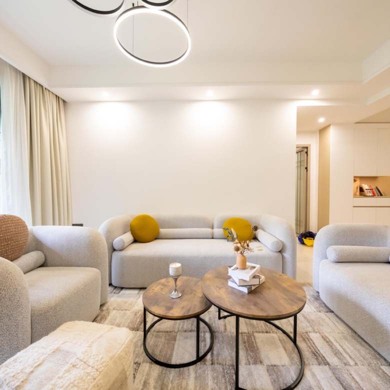 Rhapta One Residency bright living room with cream sofas, round wooden coffee tables, decorative cushions, and modern ceiling lights.