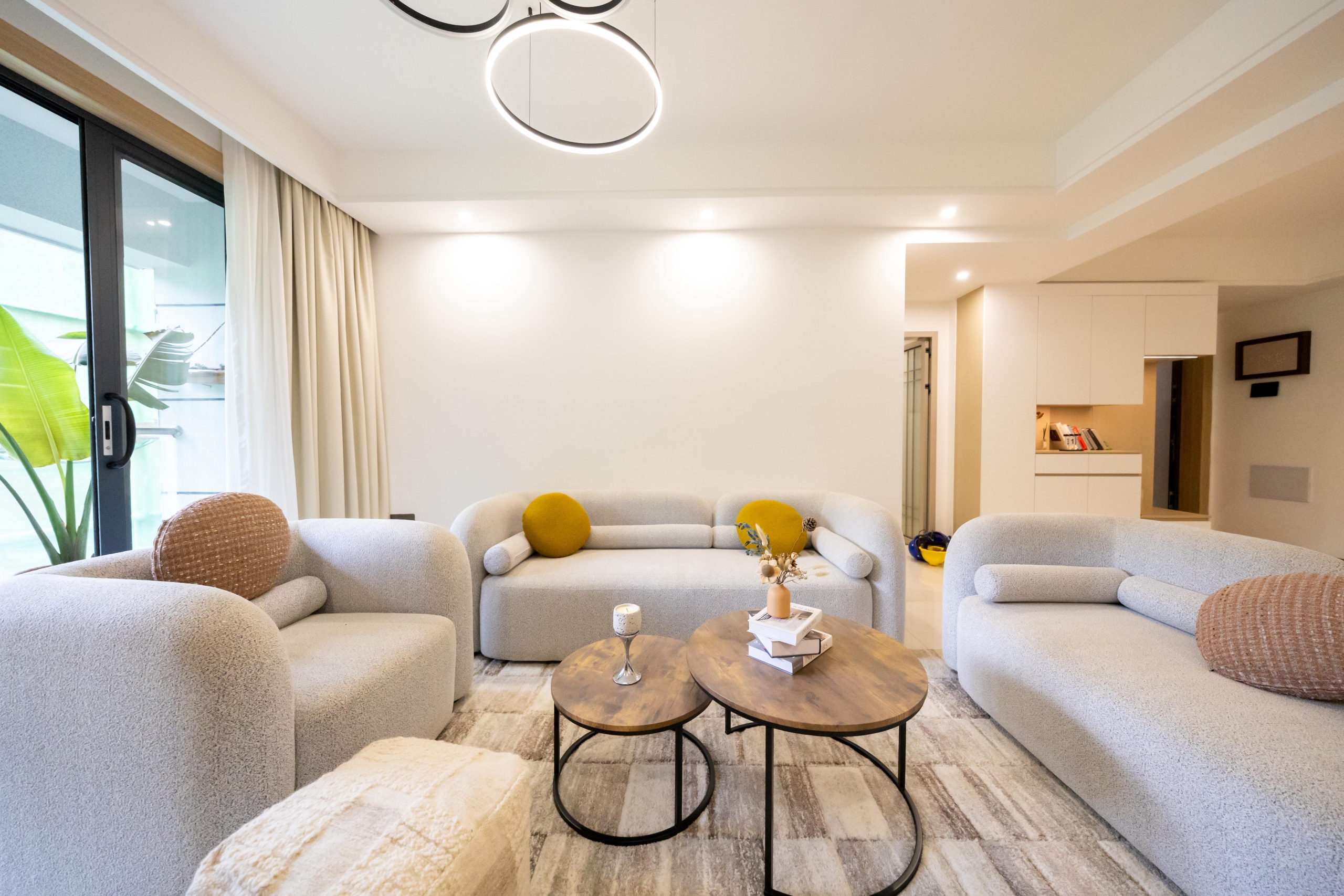 Rhapta One Residency bright living room with cream sofas, round wooden coffee tables, decorative cushions, and modern ceiling lights.