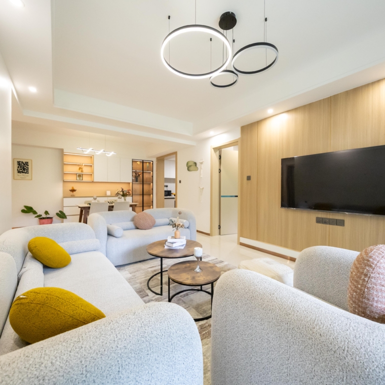 Rhapta One Residency spacious living room with curved cream sofas, wooden feature TV wall, circular chandeliers, and dining area.