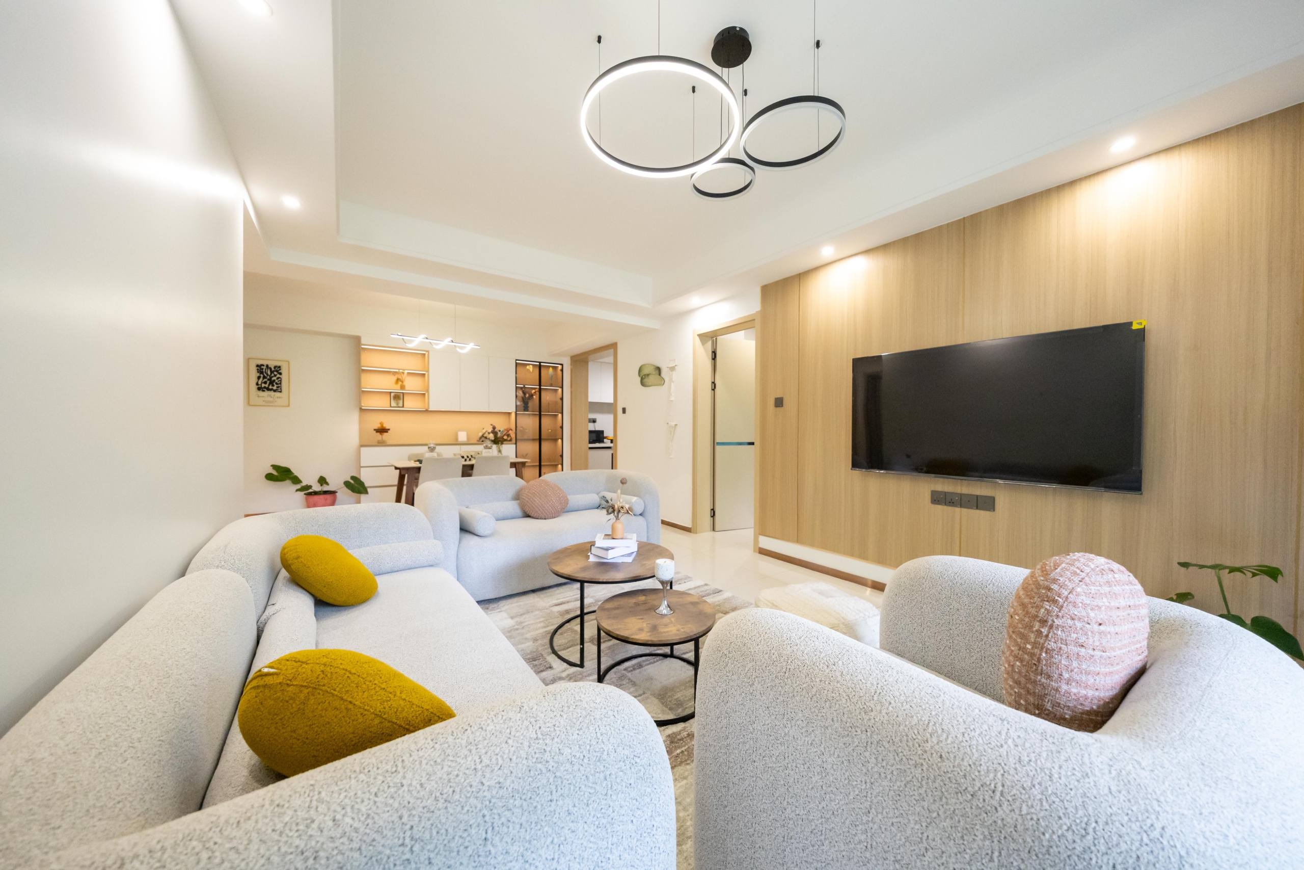 Rhapta One Residency spacious living room with curved cream sofas, wooden feature TV wall, circular chandeliers, and dining area.