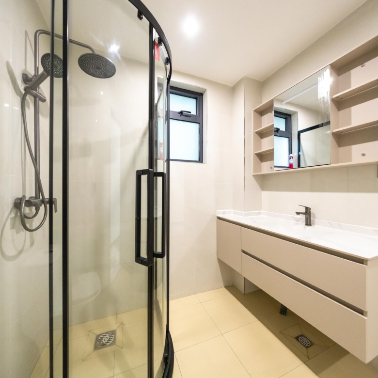Rhapta One Residency modern bathroom with black-framed glass shower, rainfall showerhead, floating vanity, mirrored cabinet, and tiled flooring.