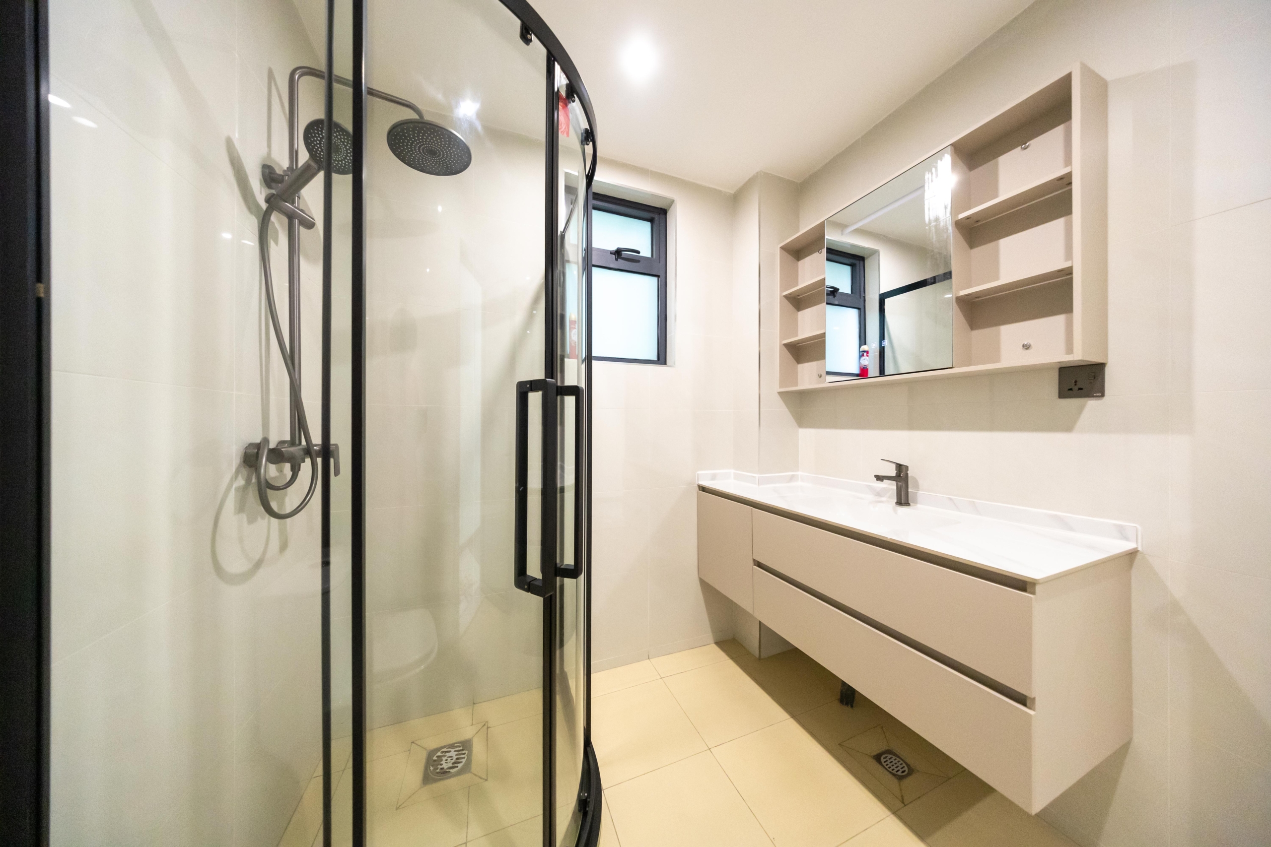 Rhapta One Residency modern bathroom with black-framed glass shower, rainfall showerhead, floating vanity, mirrored cabinet, and tiled flooring.