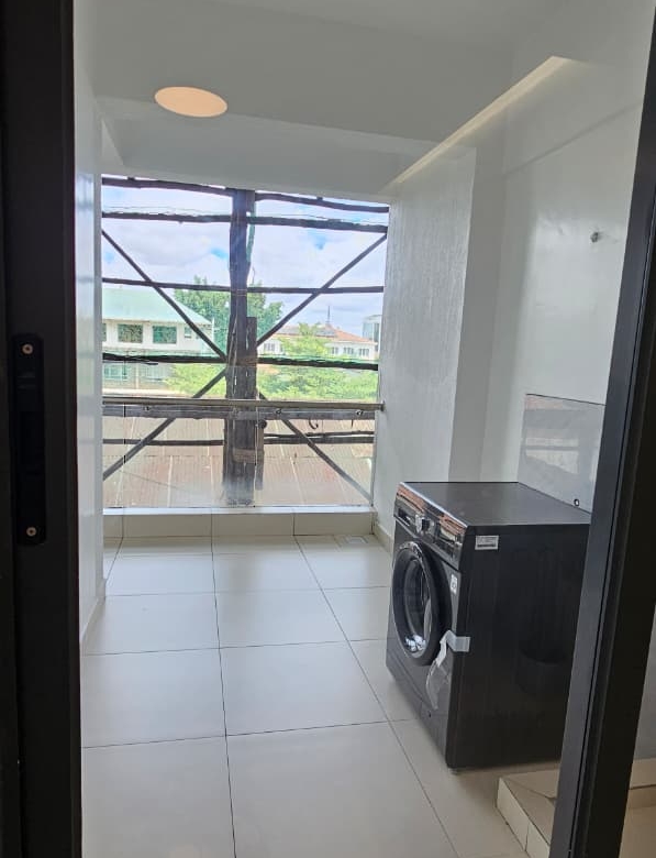 Ilu Green Homes apartment laundry area featuring a front-loading washing machine, tiled flooring, large windows, bright natural lighting, and a dedicated utility space.