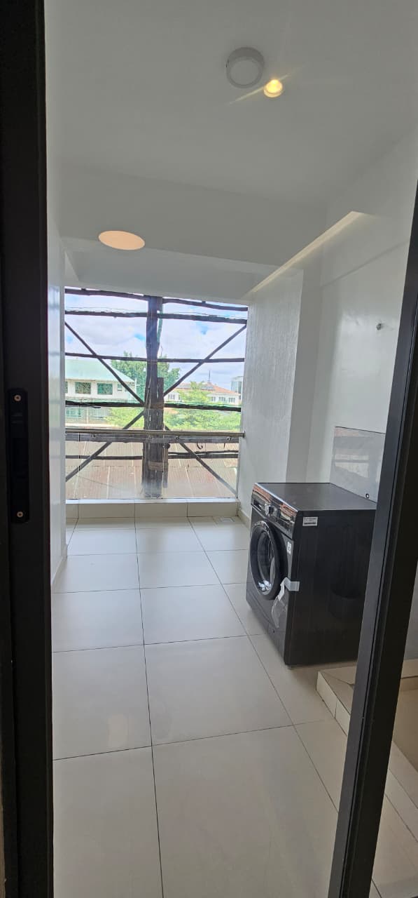 Ilu Green Homes apartment laundry area featuring a front-loading washing machine, tiled flooring, large windows, bright natural lighting, and a dedicated utility space.