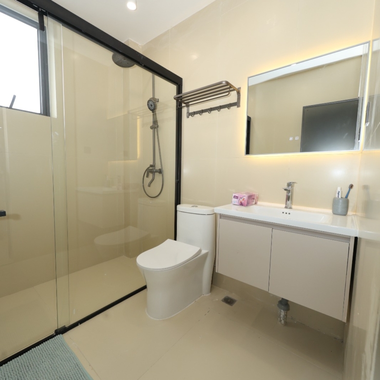 Bright apartment bathroom with vanity and glass shower at Luster Arbor Residency