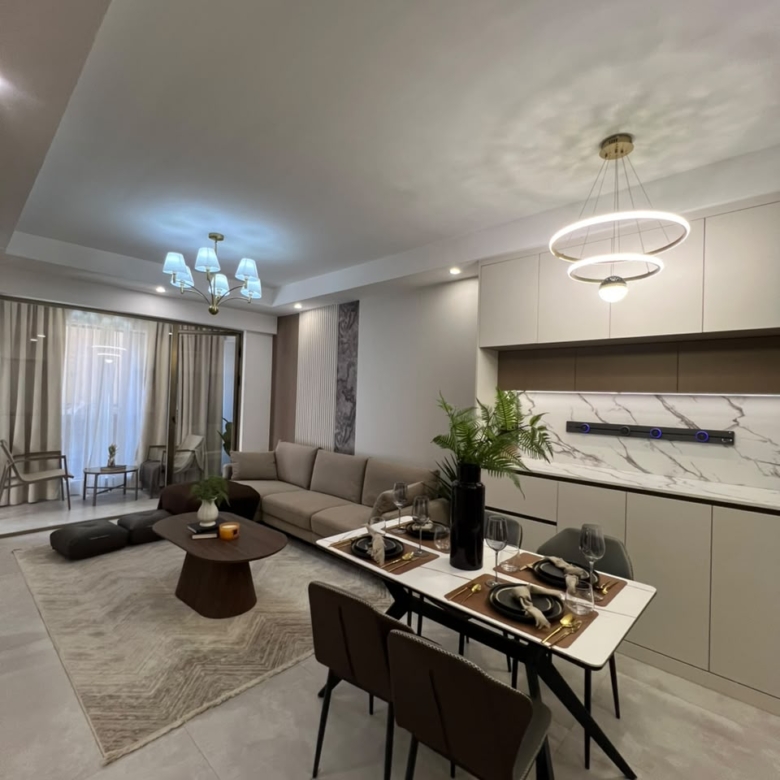 Express View Residency spacious living and dining room featuring white sofas, contemporary dining furniture, decorative pendant lights, wood-panelled walls, and large sliding glass doors.