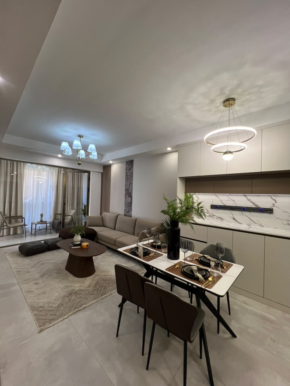 Express View Residency spacious living and dining room featuring white sofas, contemporary dining furniture, decorative pendant lights, wood-panelled walls, and large sliding glass doors.