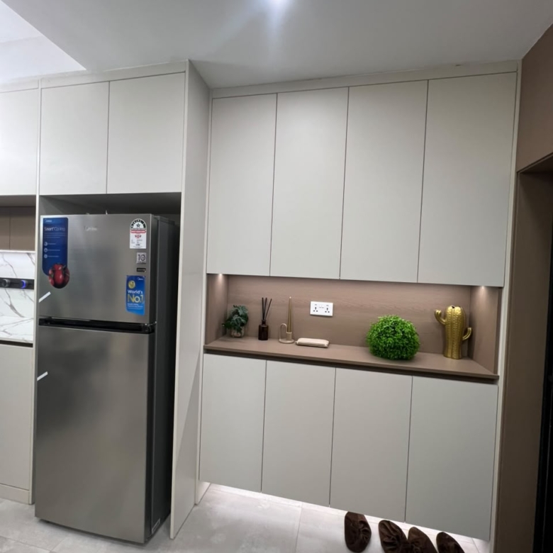 Express View Residency modern kitchen storage area featuring a stainless steel refrigerator, floor-to-ceiling fitted cabinets, illuminated countertop, and decorative open shelving.