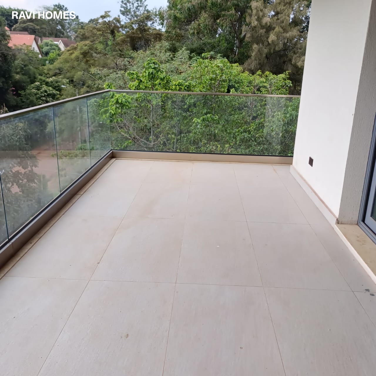 Garden Villas Lavington spacious tiled balcony with transparent glass railings, white exterior walls and views of green trees.