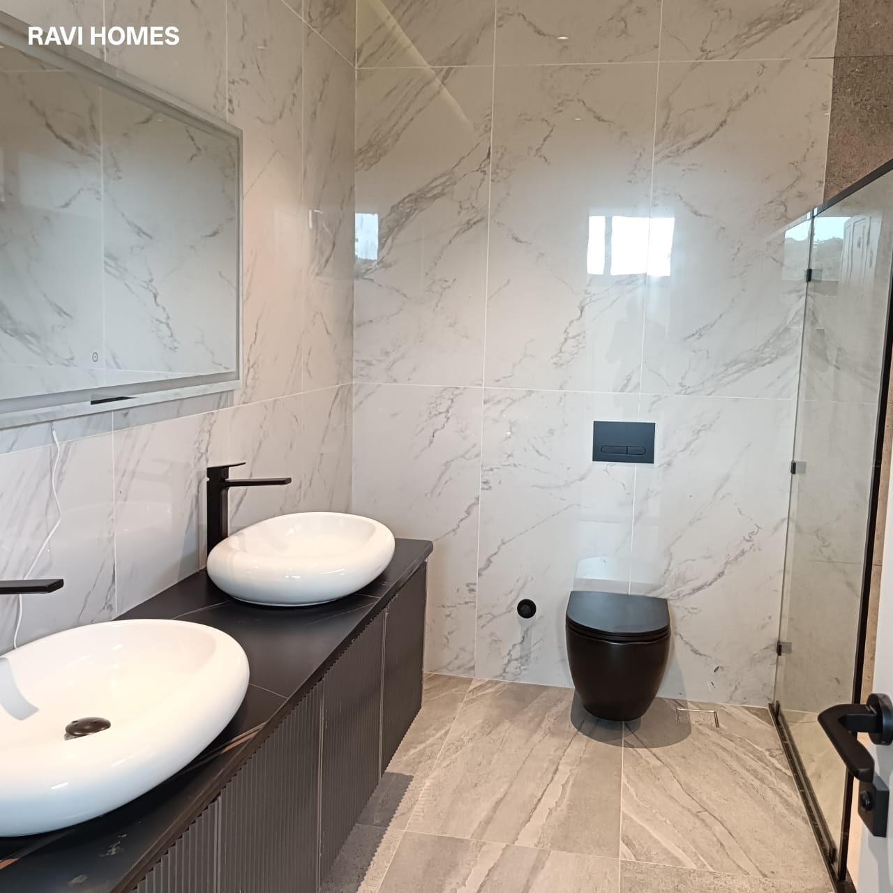 Garden Villas Lavington modern bathroom with marble-effect wall tiles, double vessel sinks, dark vanity cabinets, black fixtures and glass shower enclosure.