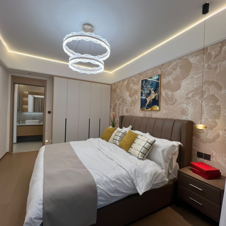 Longines Bay bedroom with fitted wardrobes, upholstered bed, modern chandelier and ensuite bathroom access.