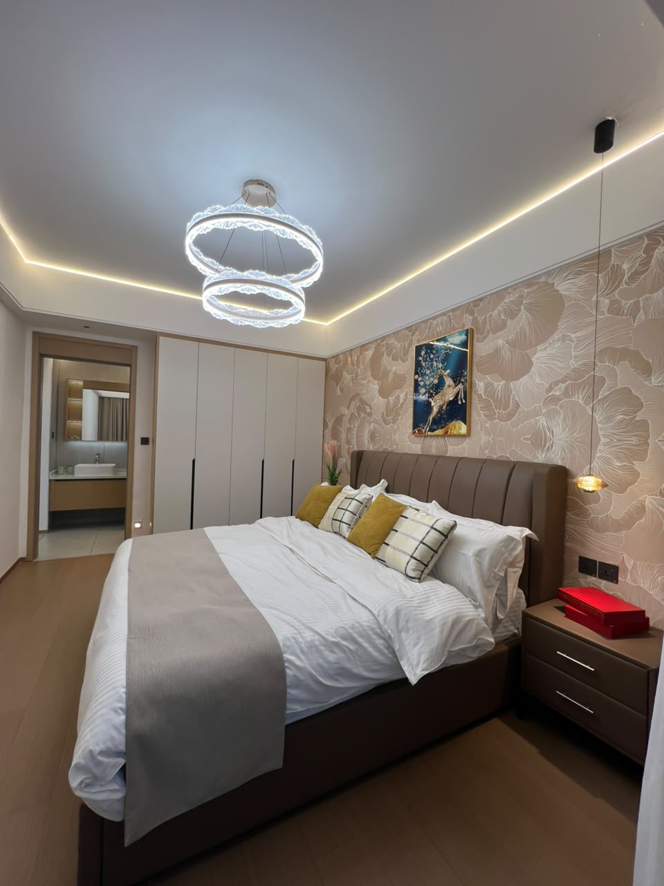 Longines Bay bedroom with fitted wardrobes, upholstered bed, modern chandelier and ensuite bathroom access.