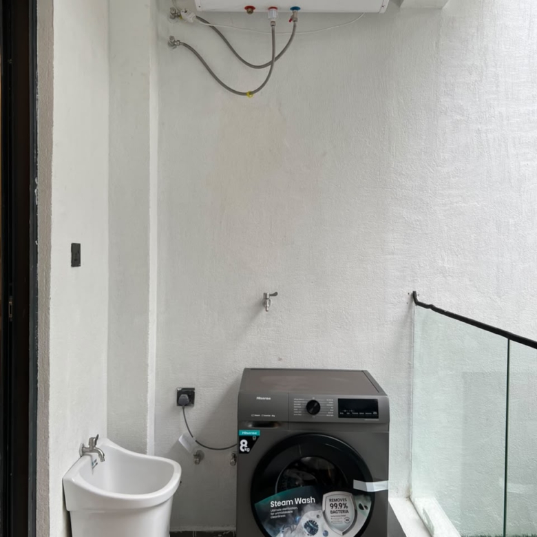 Longines Bay apartment laundry area with washing machine, utility sink, water heater and glass balcony railing.