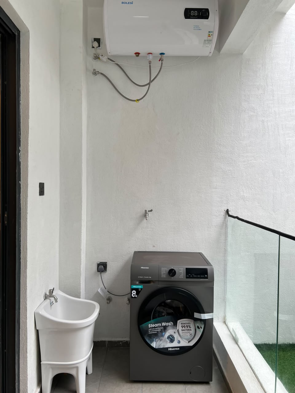 Longines Bay apartment laundry area with washing machine, utility sink, water heater and glass balcony railing.