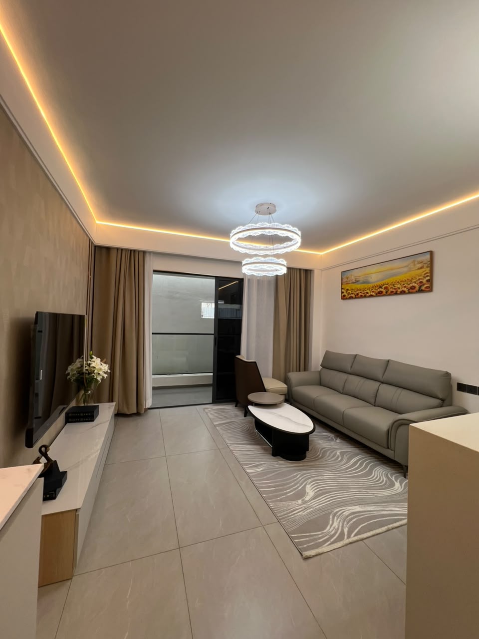 Longines Bay living room with modern sofa, decorative chandelier, tiled flooring and sliding balcony doors.