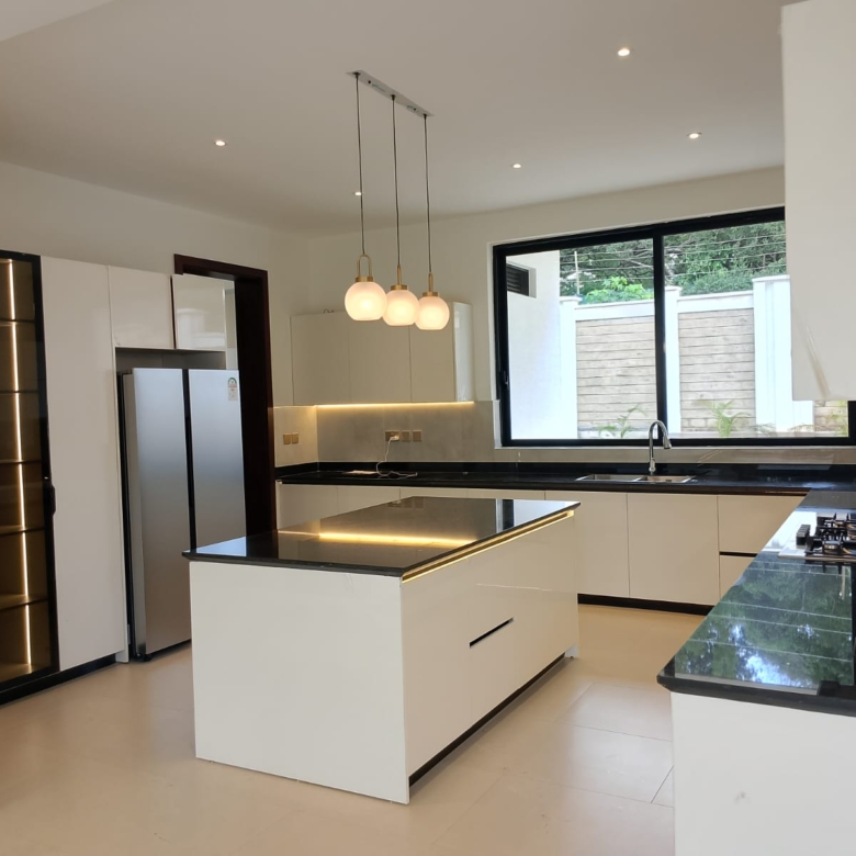 Radiant Villas luxury modern kitchen in Westlands Nairobi featuring central island, fitted cabinets, black countertops and cooking appliances.