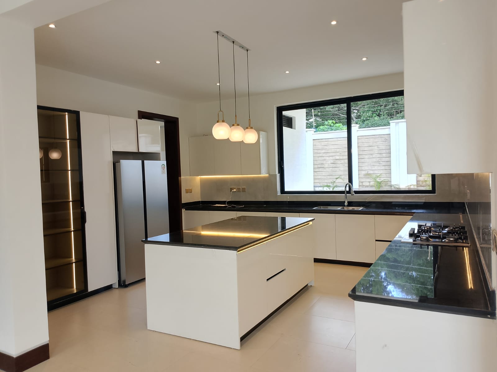 Radiant Villas luxury modern kitchen in Westlands Nairobi featuring central island, fitted cabinets, black countertops and cooking appliances.